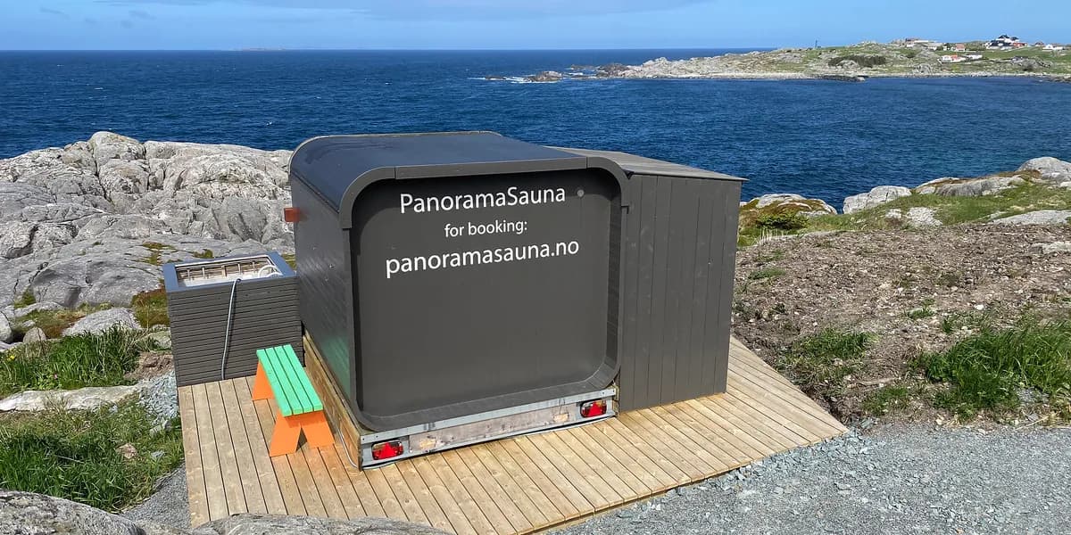 PanoramaSauna – eksterior PanoramaSauna sett utanfrå på svaberg ved sjøen ein solskinsdag, med teksten «PanoramaSauna – for booking: panoramasauna.no» på sida