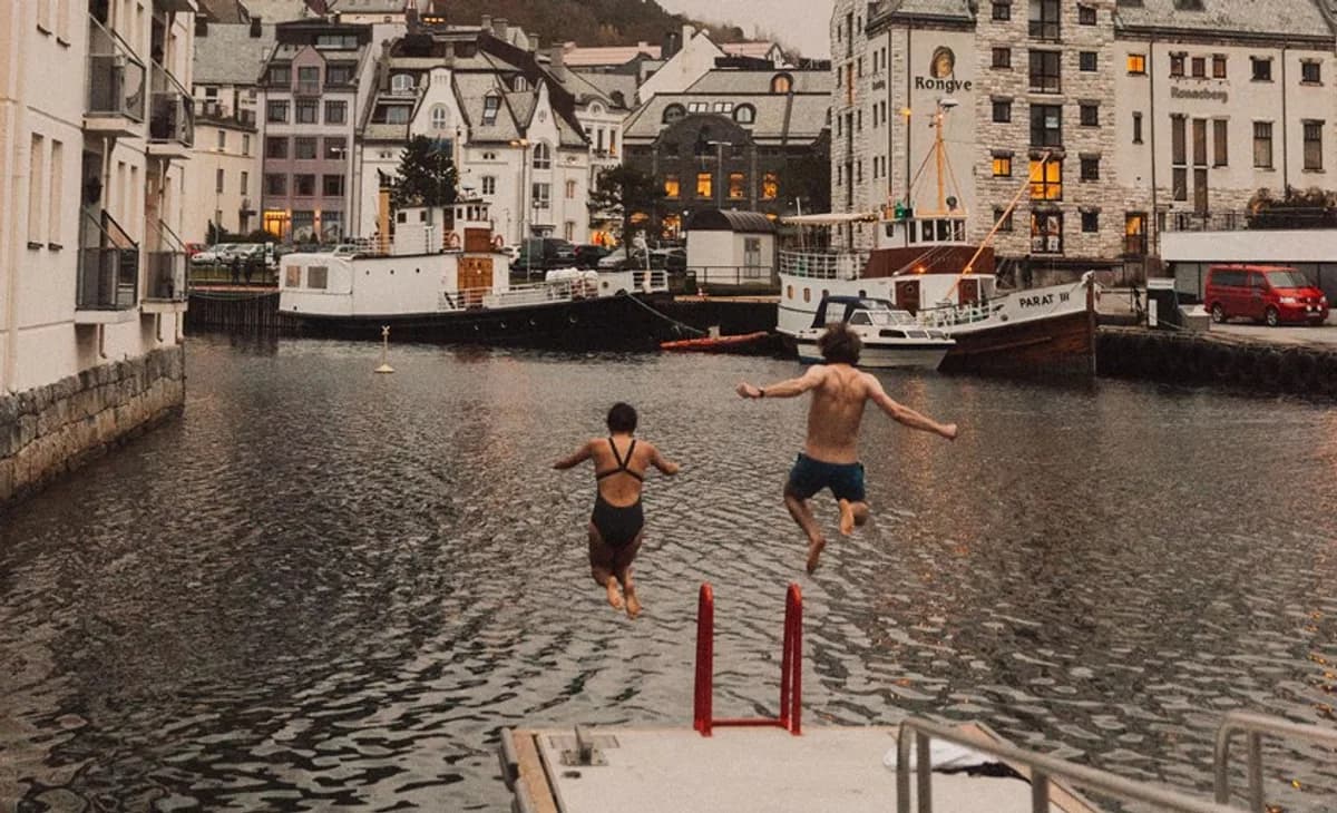 To personer hopper i sjøen fra flytebryggen ved Brosundet badstue i Ålesund