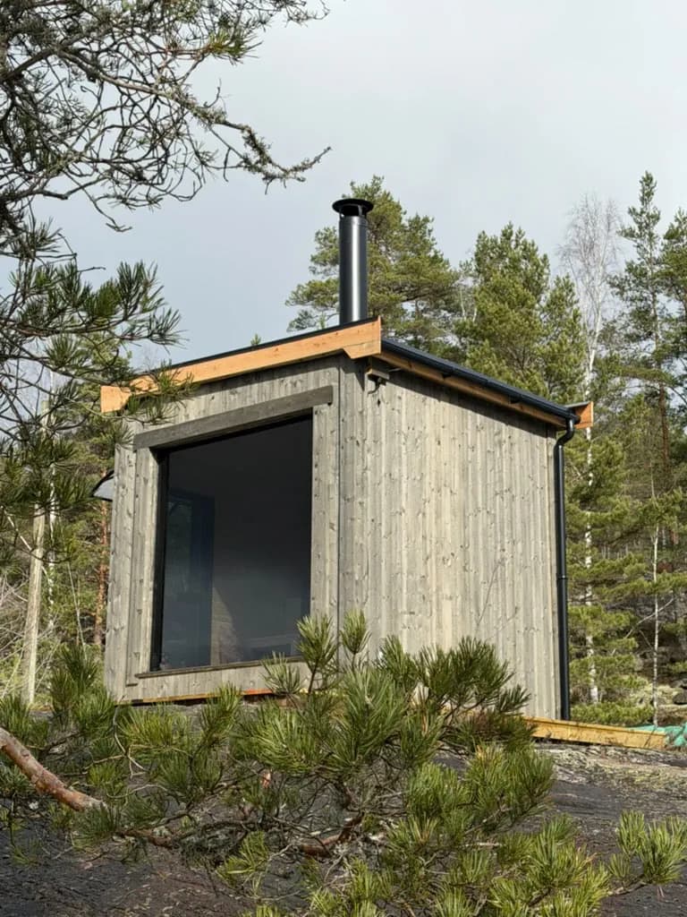 Badstuens tre-eksteriør med pipe, omgitt av skog