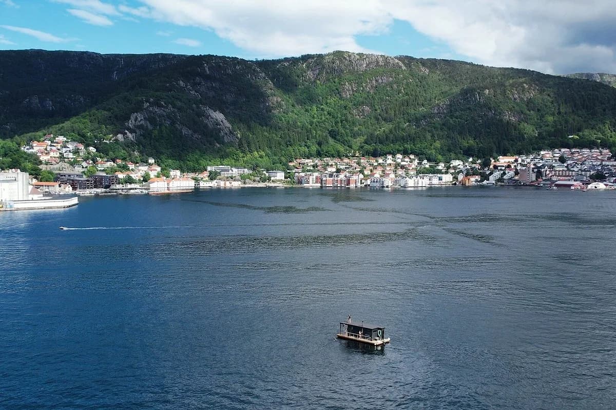 Flytende saunabåt fra City Sauna Bergen seiler på fjorden med byfjellene bak