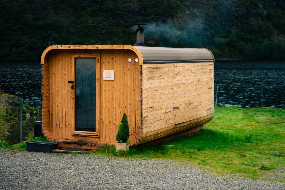 Vedfyrt badstue ved Grimevatnet i Bergen med røyk fra pipa og fjell i bakgrunnen