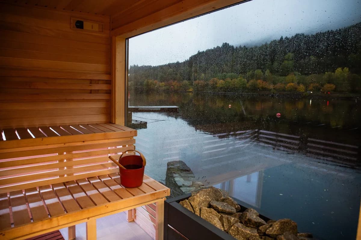 Interiør av Heit Kongen Sauna i Bergen med trebenker og panoramautsikt over Nordåsvannet gjennom stort vindu