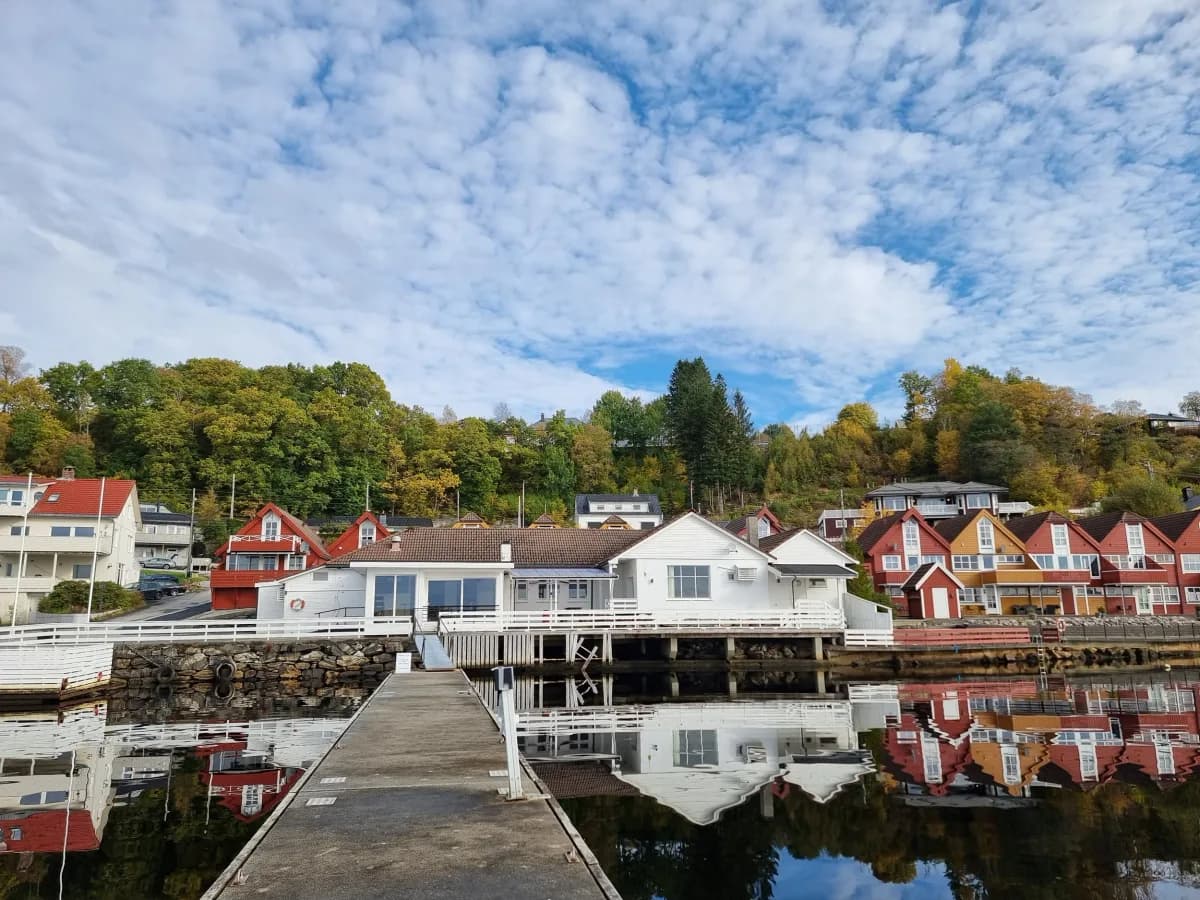 Lindås Sjøbad sett fra bryggen med hvite sjøhus og fargerike bolighus langs vannet i Lindås