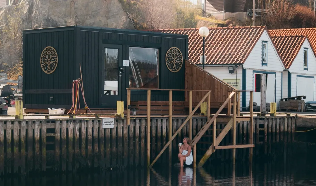 Vestfjord Sauna - Hjellestad – interior Interiør i badstuen med utsikt over småbåthavnen på Hjellestad gjennom stort vindu, ovn med stein i forgrunnen