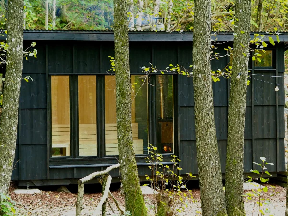Skogsbad Høyåsen saunabygg i mørkt tre med store glassvinduer omgitt av skog i Bjorbekk
