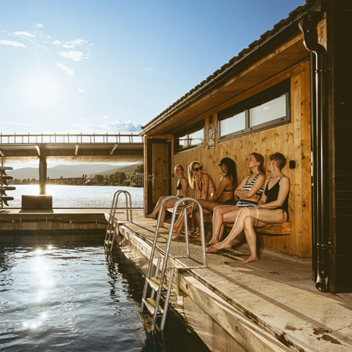 Gjester på terrassen til flytende badstue Ælvebadstua ved Drammenselva en solrik dag