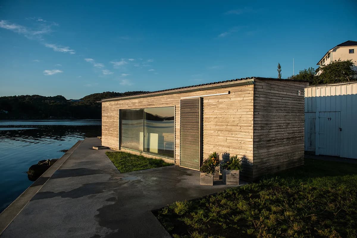 Farsund Badehus sett utenfra ved fjorden i kveldslys, moderne trebygg i Farsund