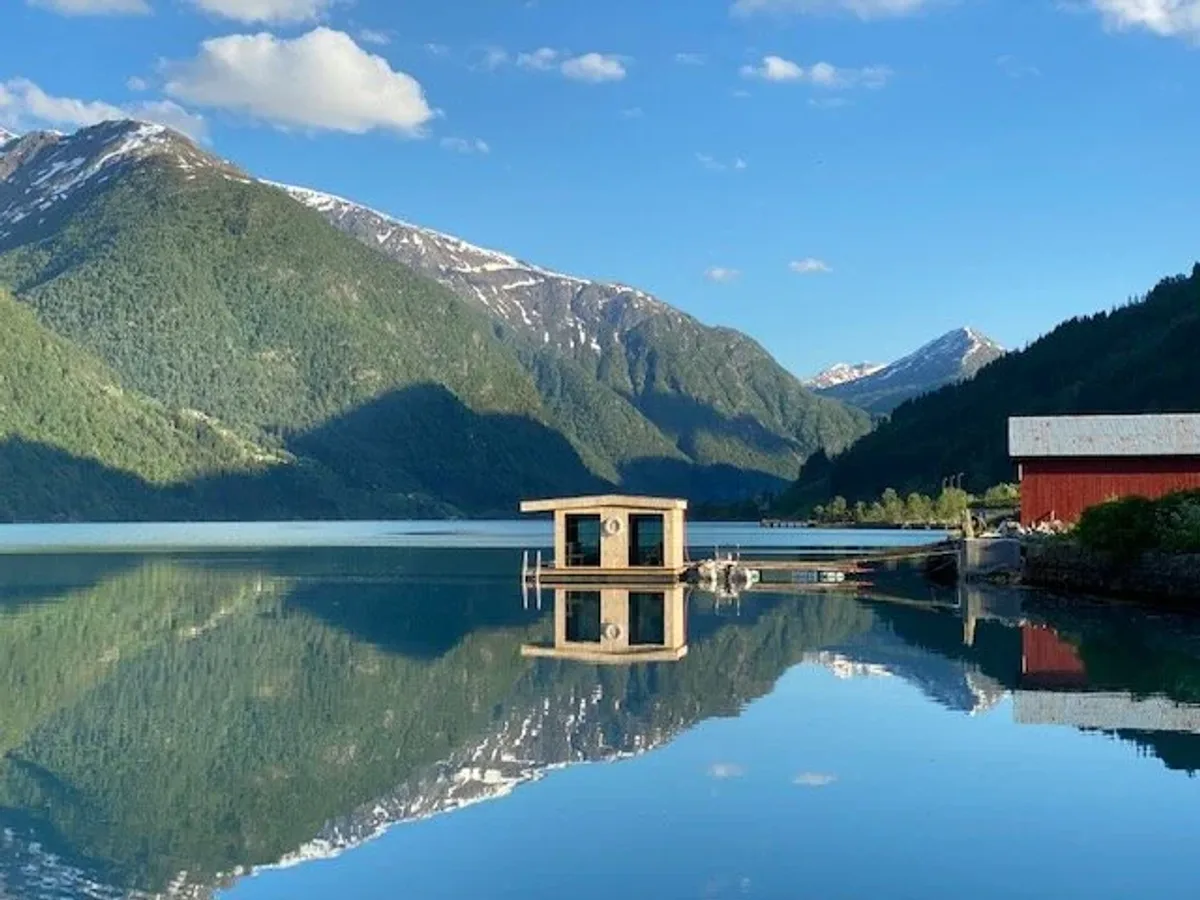 Dampen flytande badstu på Fjærlandsfjorden med fjell og spegelblank fjord i Fjærland