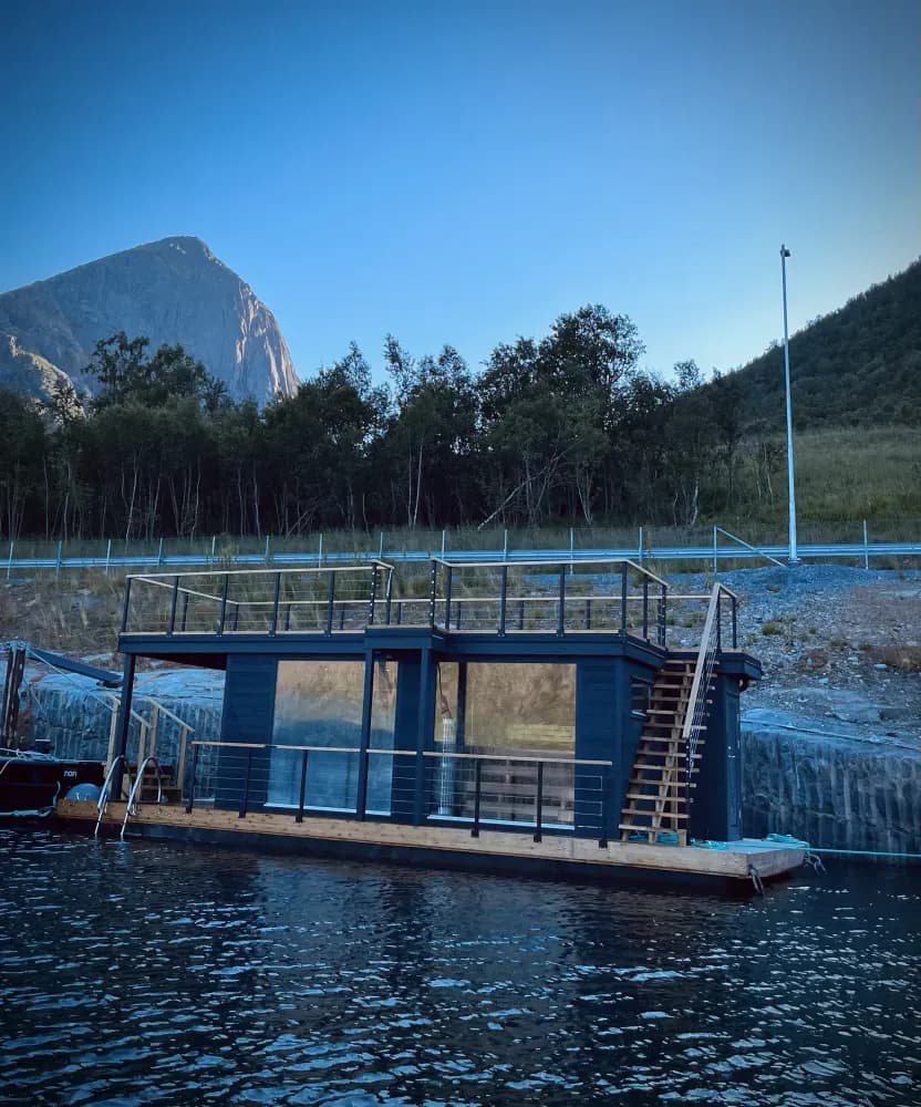 Damperiet Sauna i Fjordgård sett fra sjøen – flytende badstue med glassfasade, takterrasse og fjell i bakgrunnen