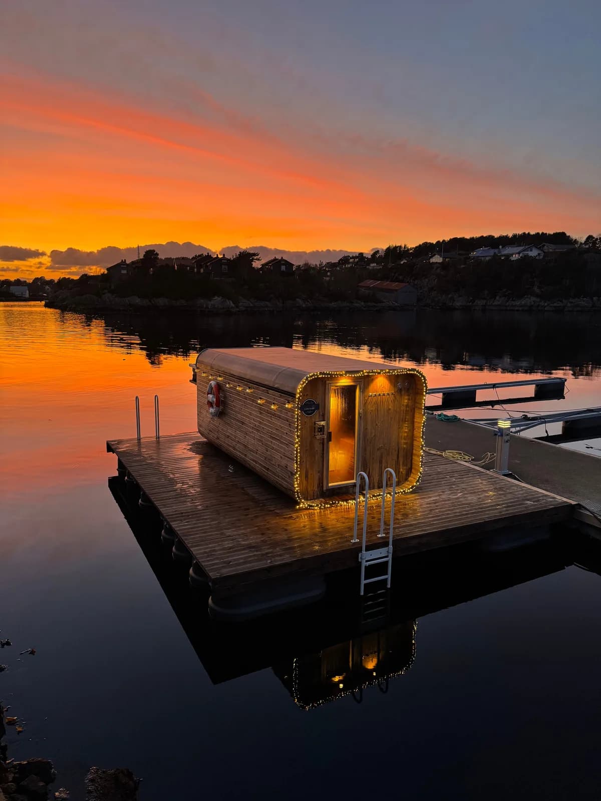Flytande badstue Kinn Damp i Florø ved solnedgang med lyslenker og speglblankt vatn