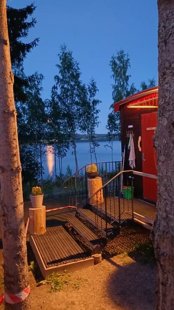 Badstuebygg i rødt panel med tent lys om kvelden, ved bredden av Mjøsa