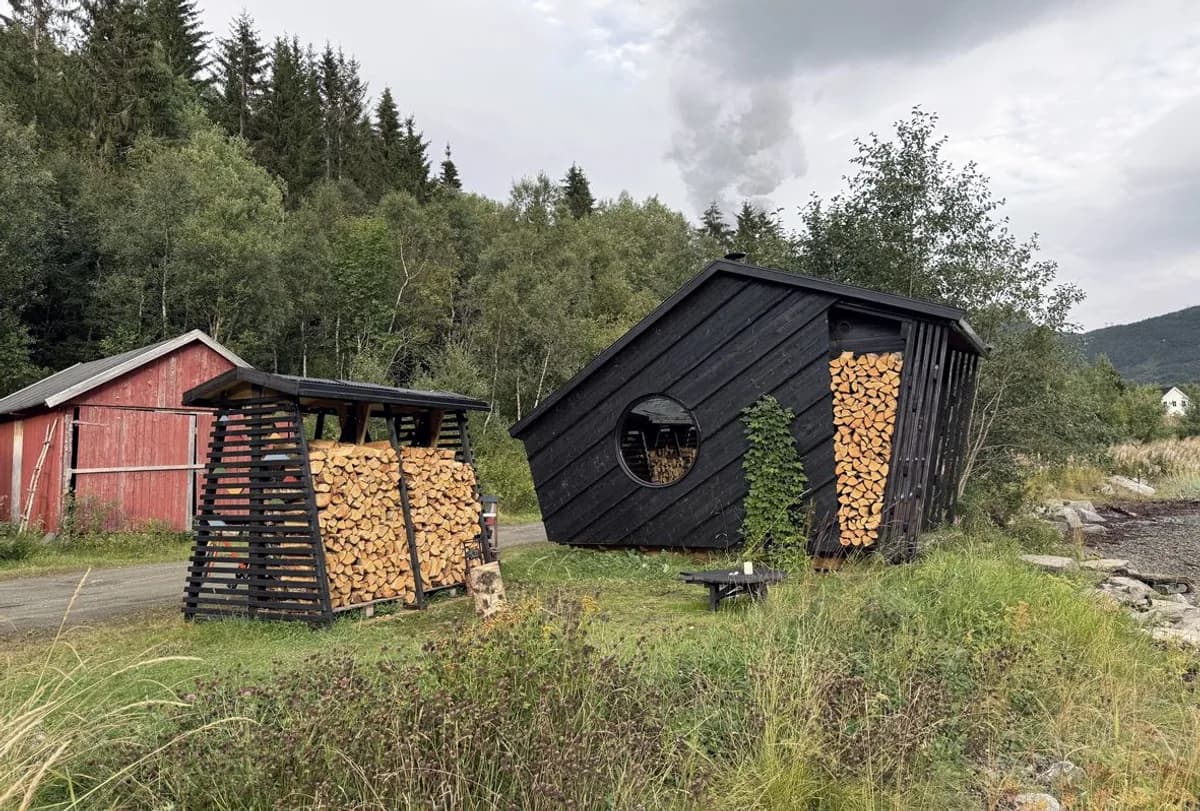 Grjotangr Sauna i Gratangsbotn, svartmalt vedfyrt badstue med vedstabler langs veggene