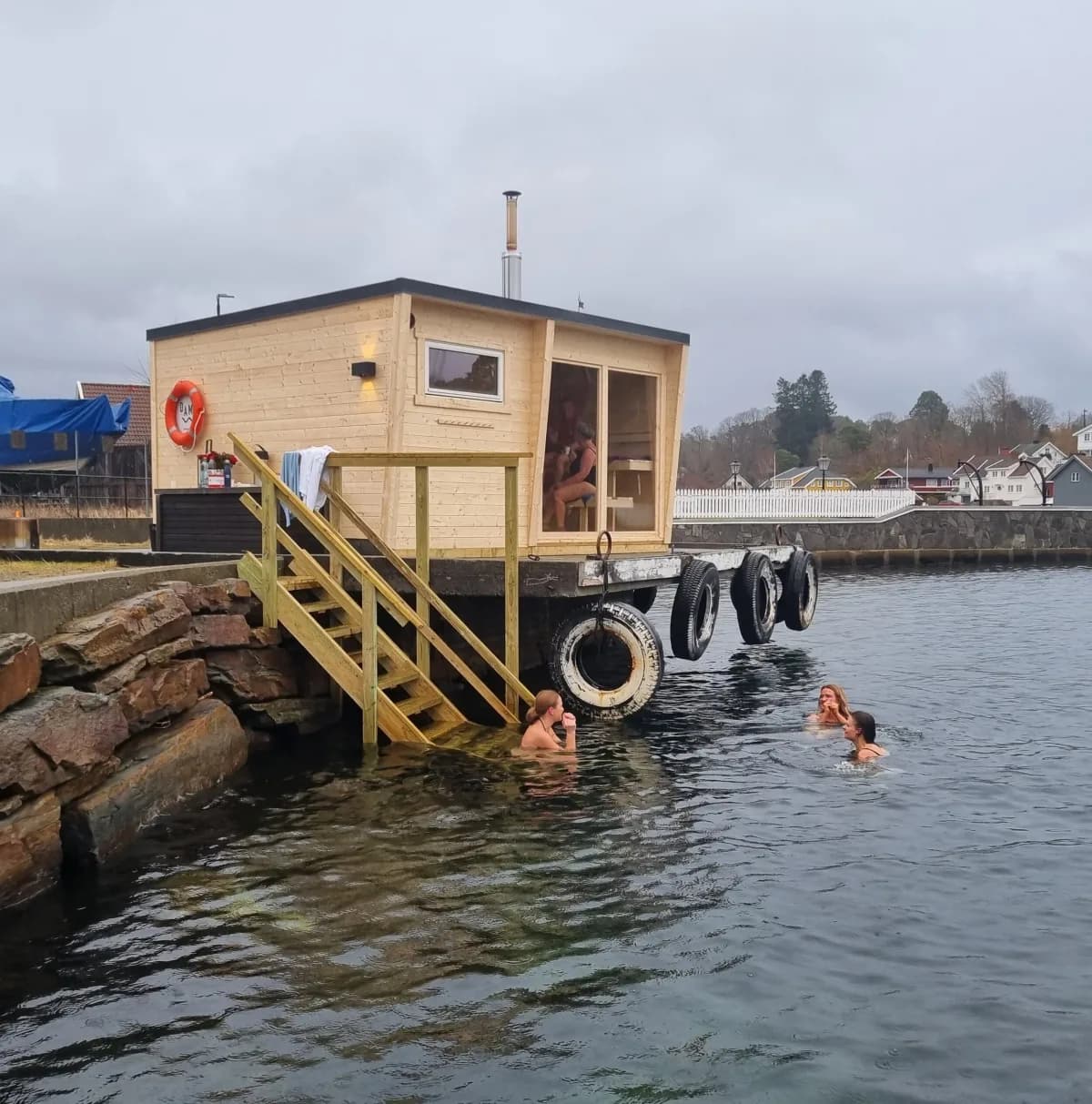 Flytende badstue Damp Fevik ved brygga i Fevikkilen med badende gjester i sjøen