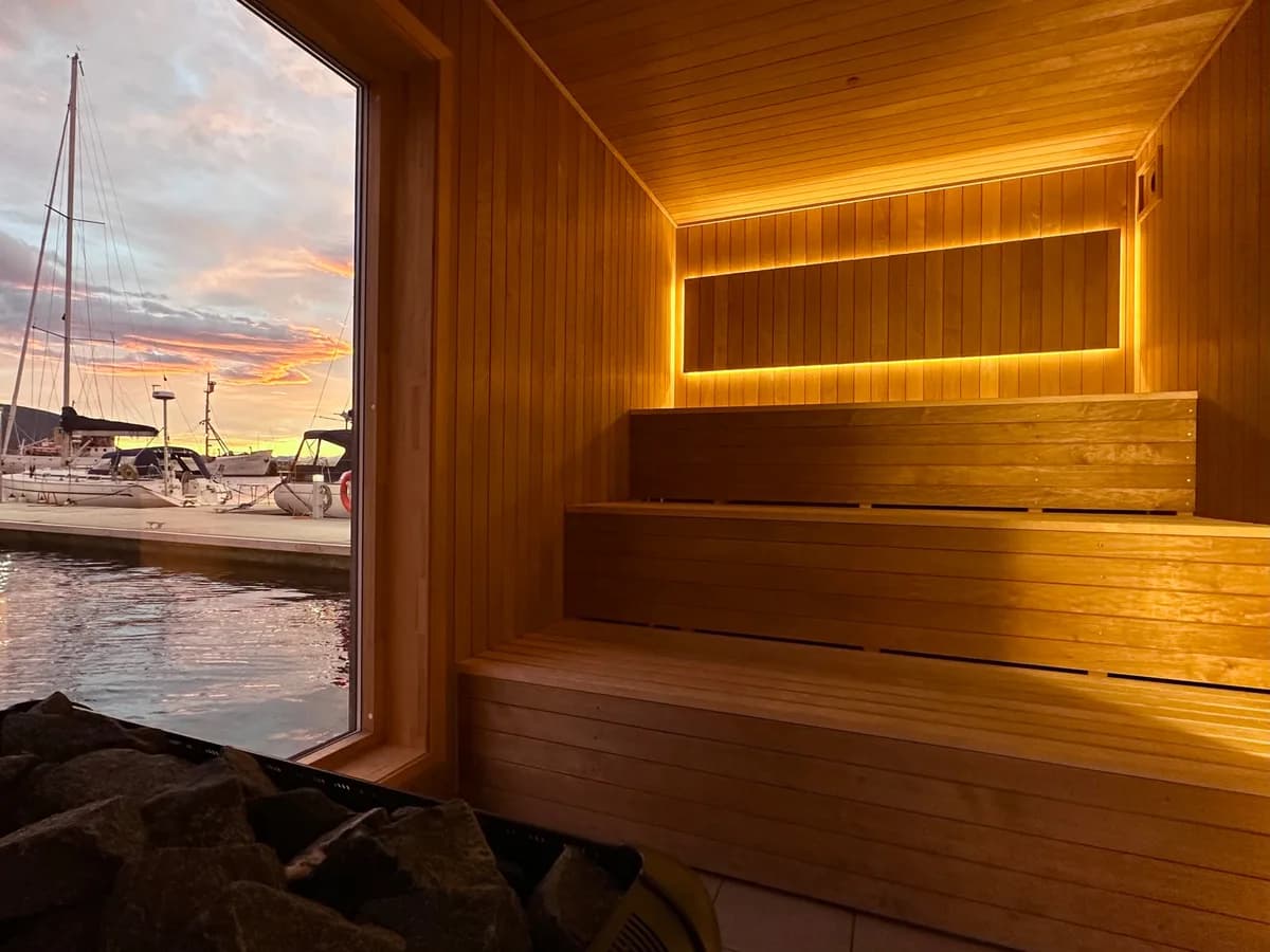 Interiør i Hareid Fjordsauna med trebenker, varm belysning og utsikt over marinaen i Hareid