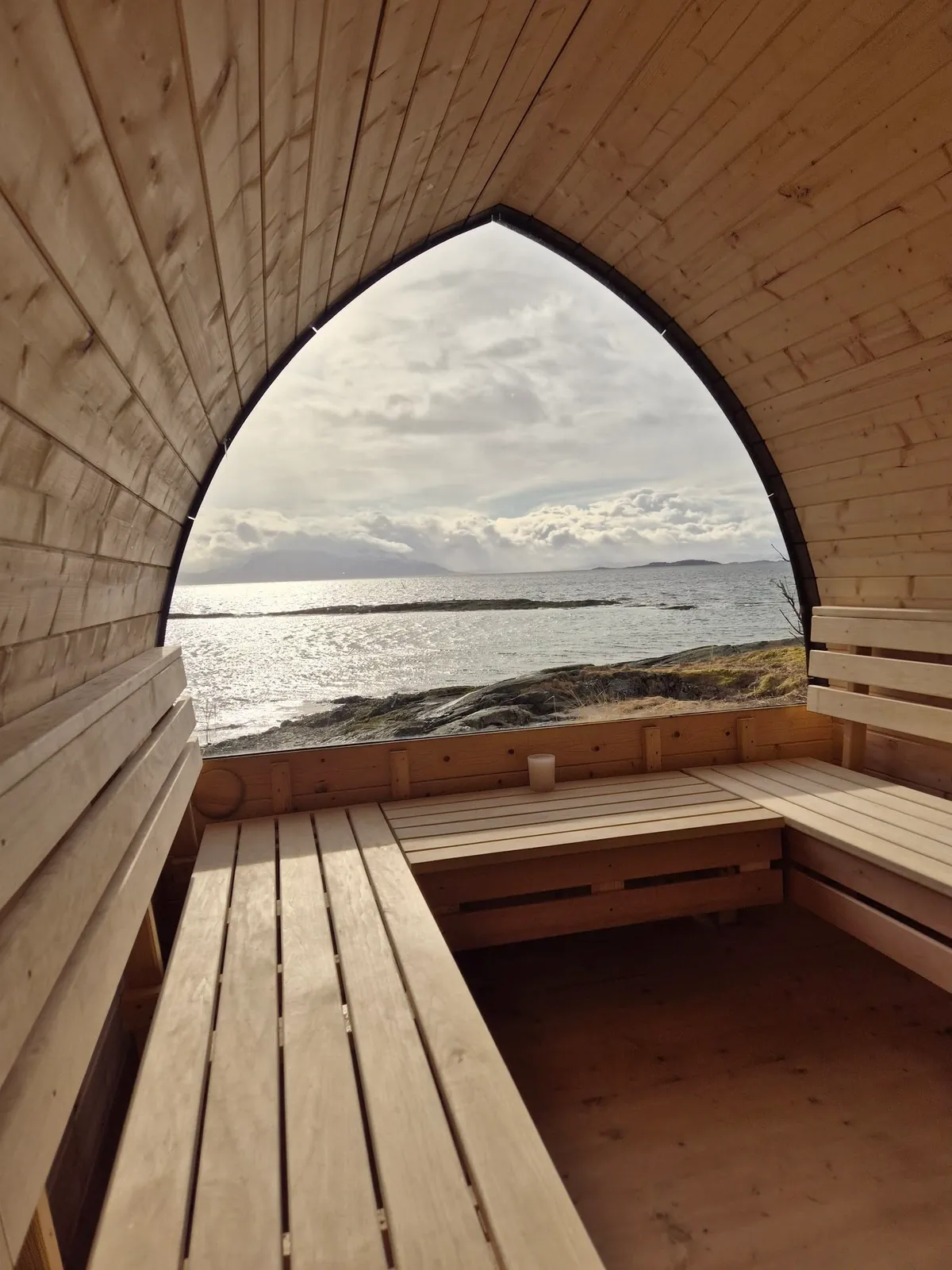 Interiør i Heitlaugen Badstu på Grytøya med trebenker og spissbuet vindu med utsikt over havet og fjellene