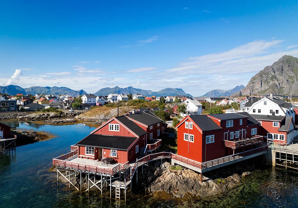 Røde rorbuer på stolper over sjøen ved Henningsvær Rorbuer i Lofoten med fjell i bakgrunnen