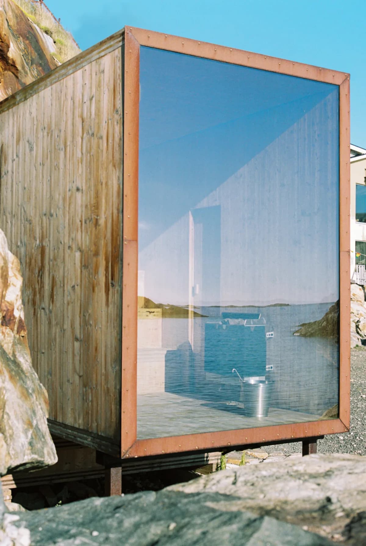 Trevarefabrikken Sauna i Henningsvær sett utenfra med havneområdet reflektert i panoramavinduet