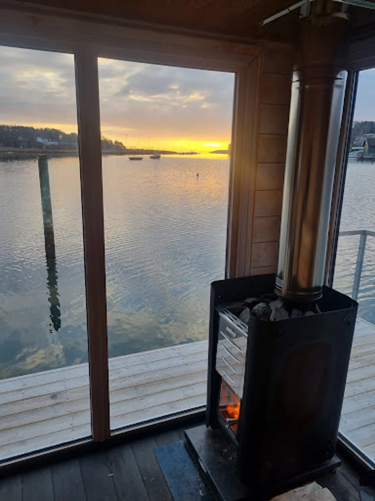 Interiør av Varmr Sauna i Husøysund med vedfyrt ovn og solnedgang over sjøen