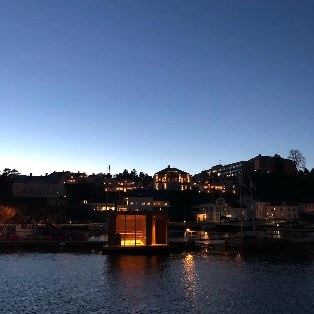 Flytende badstue fra Kragerø Badstuforening opplyst om kvelden med Kragerø sentrum i bakgrunnen