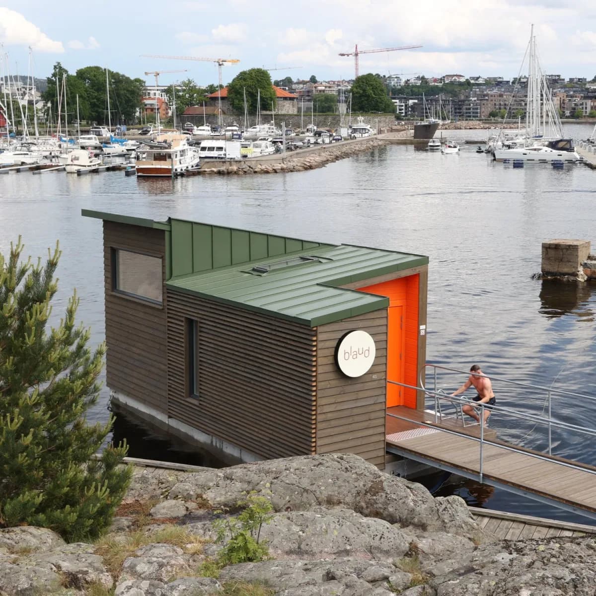 Blaud flytende badstu sett fra land ved Odderøya i Kristiansand med grønt tak og oransje dør