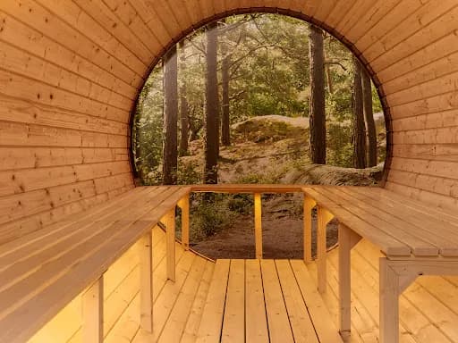 Frostglød Badstu – interior Interiør i en tønnebadstue med utsikt mot skog gjennom buet akrylglassvegg