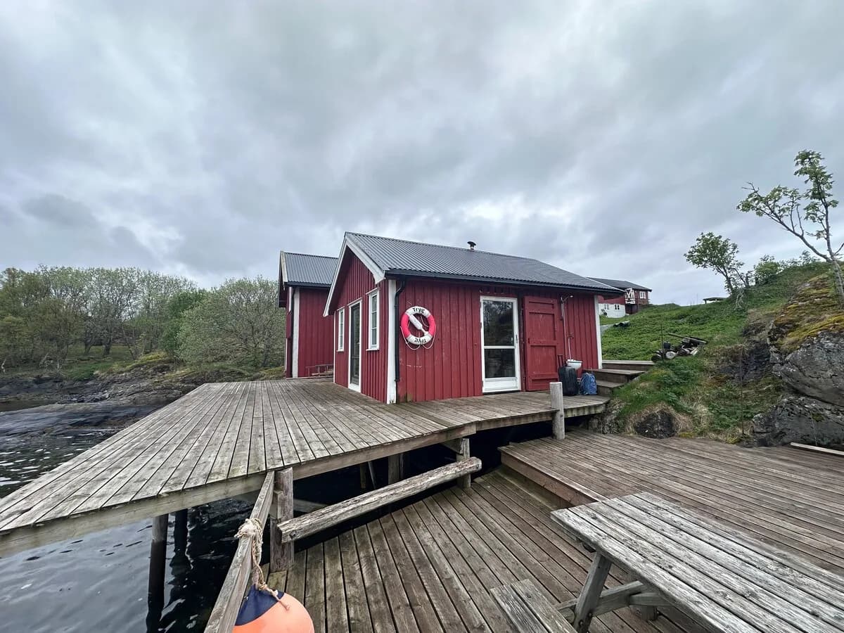 Rødt naust med badstue ved sjøen i Leirfjord, sett fra brygga med livbøye på veggen