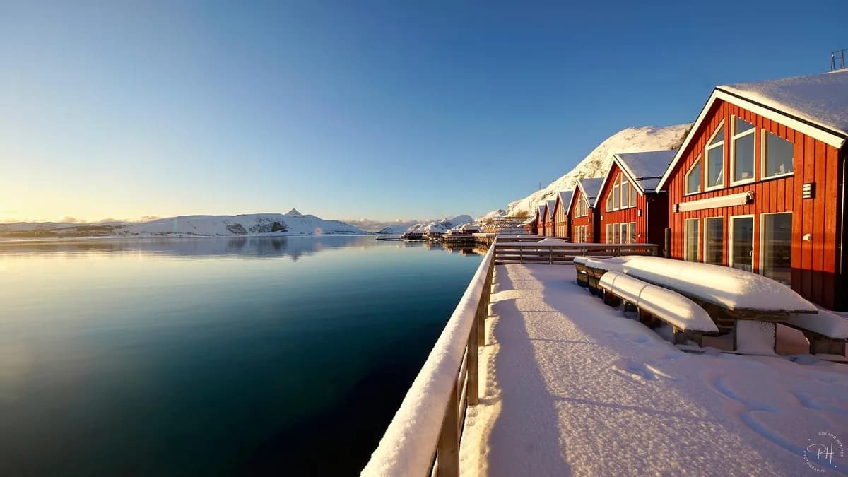 Skreda Rorbusuiter ved sjøen i Leknes med røde rorbuer og snødekte fjell i bakgrunnen