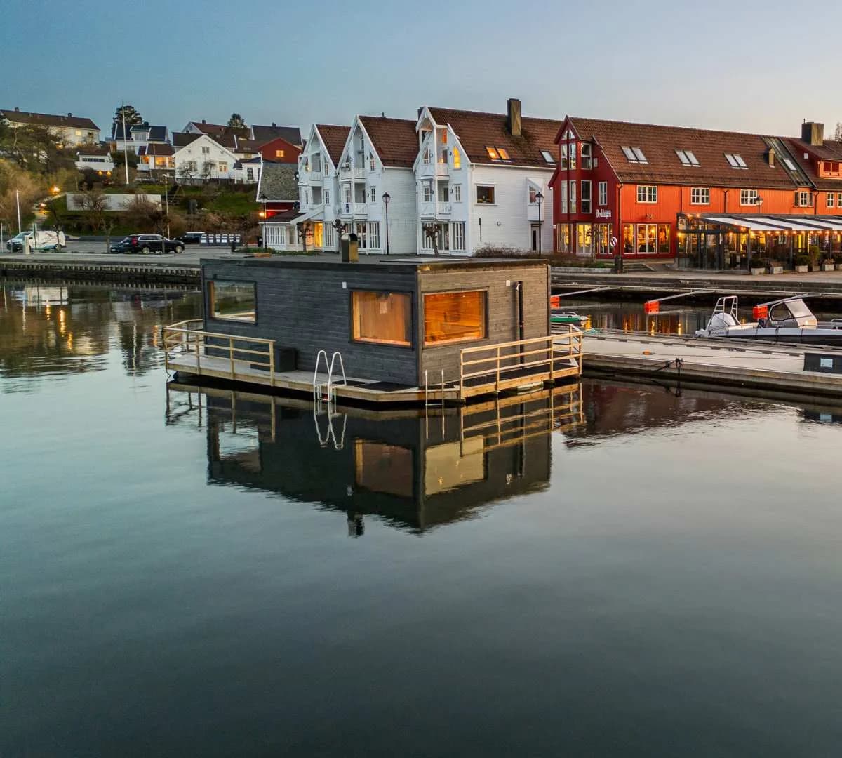 Flytende badstue Godkog i Lillesand havn i kveldslys med byen i bakgrunnen