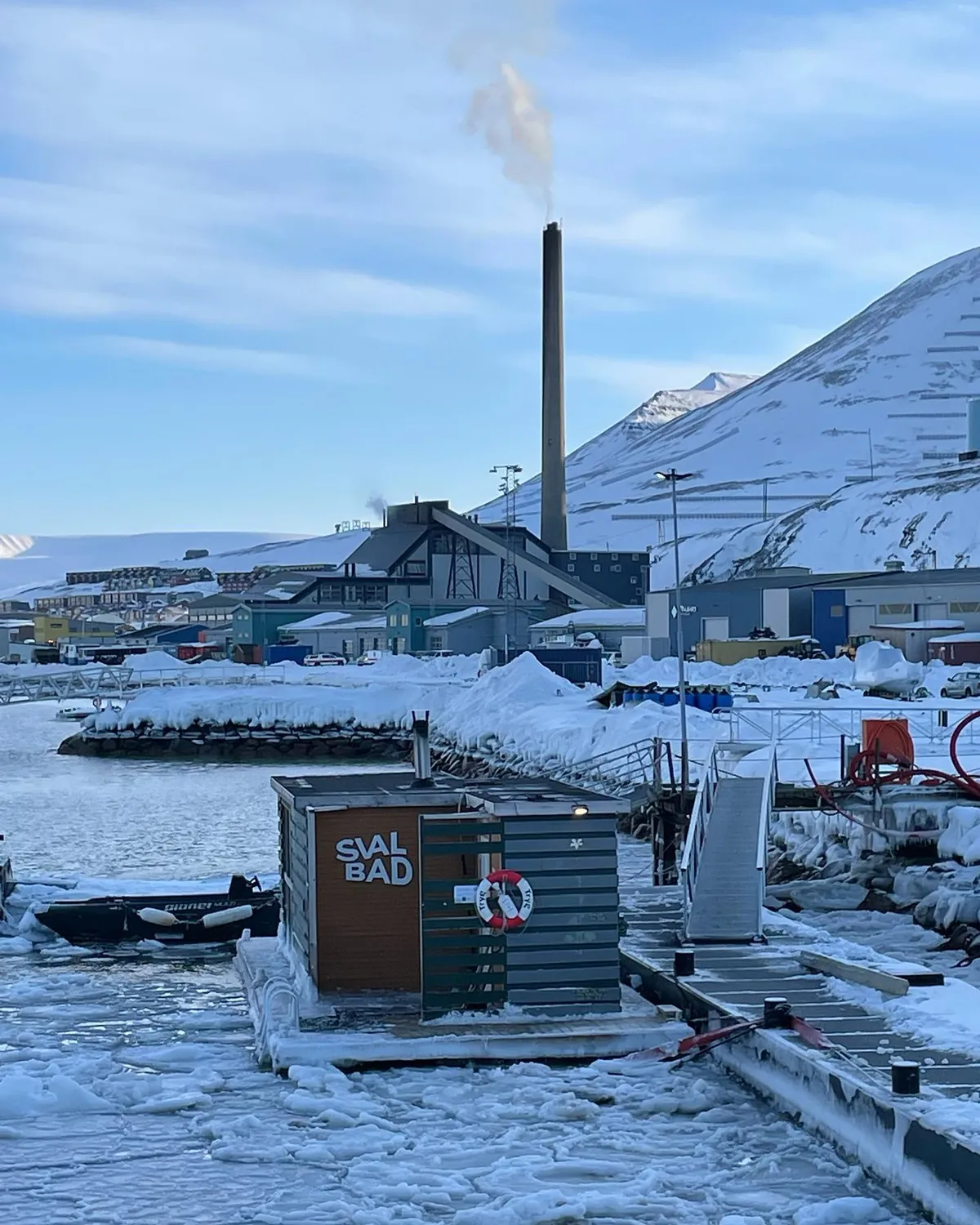SvalBad flytende badstue ved havna i Longyearbyen omgitt av is, snø og arktiske fjell på Svalbard