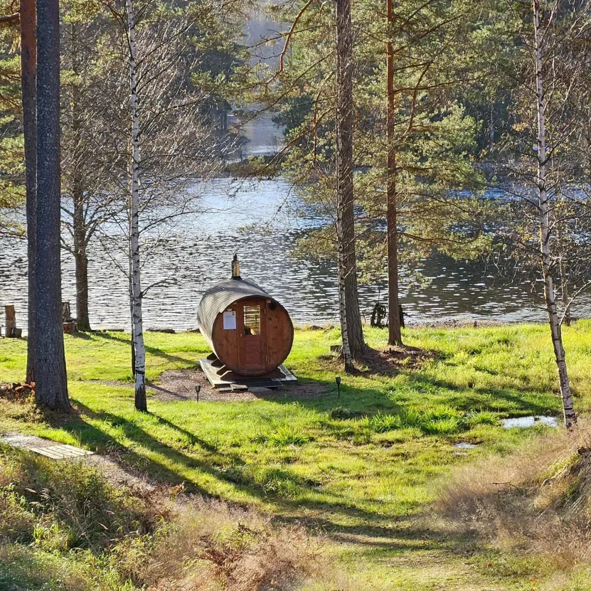 Hogga Badstulag tønnebadstu blant bjørk og furu ved Telemarkskanalen i Lunde med solglitter på vannet