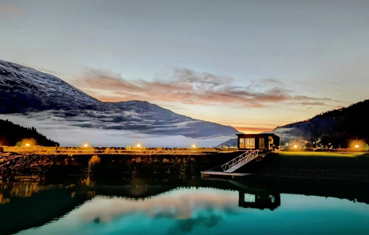 Olden Sauna ved vatnet i kveldslys med fjell og solnedgang i bakgrunnen