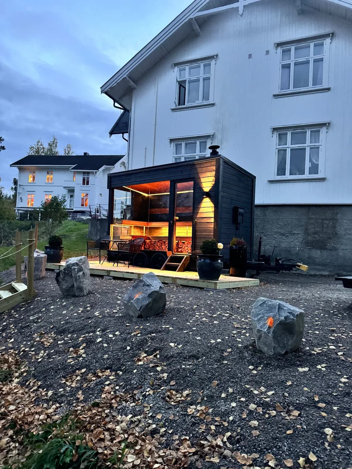 Gnist Sauna i Rena opplyst om kvelden med varm belysning og vedstabel