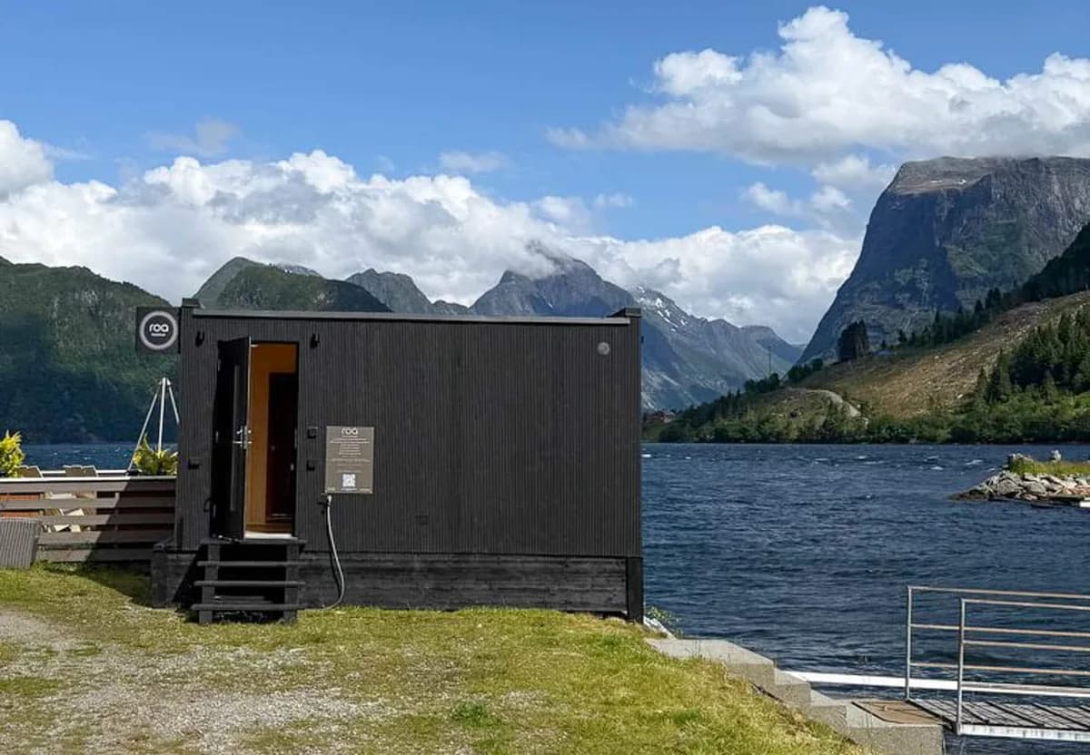 ROA Badstue Sæbø sett utenfra ved fjorden med Sunnmørsalpene i bakgrunnen