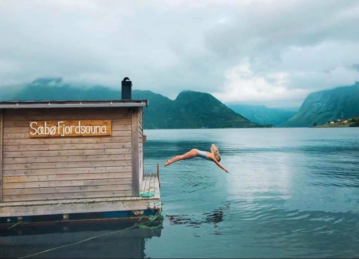 Person stuper fra Sæbø Fjordsauna ut i Hjørundfjorden med fjell i bakgrunnen
