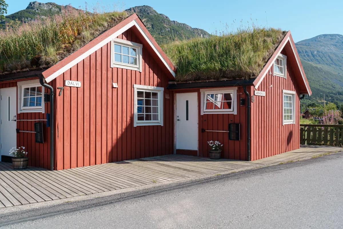 Røde sjøbuer med torvtak ved Manndalen Sjøbuer i Samuelsberg, fjell i bakgrunnen