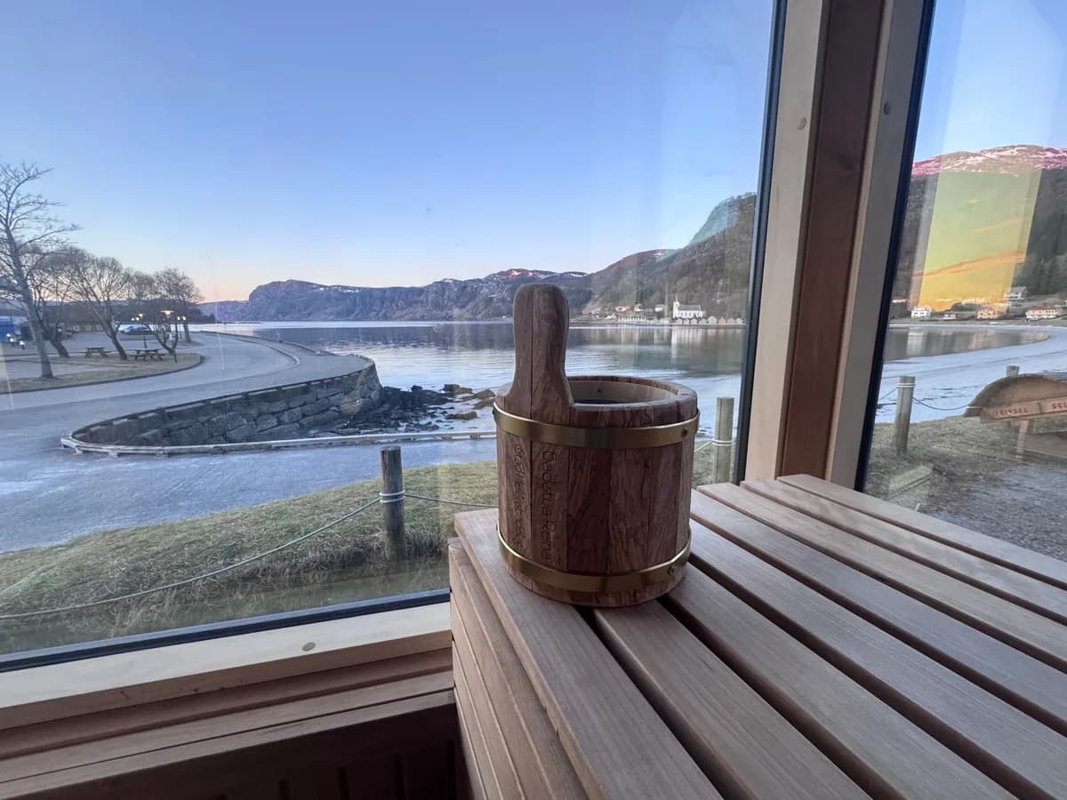 Interiør i Badstua Reina med bøtte på trebenk og panoramautsikt over fjorden i Selje