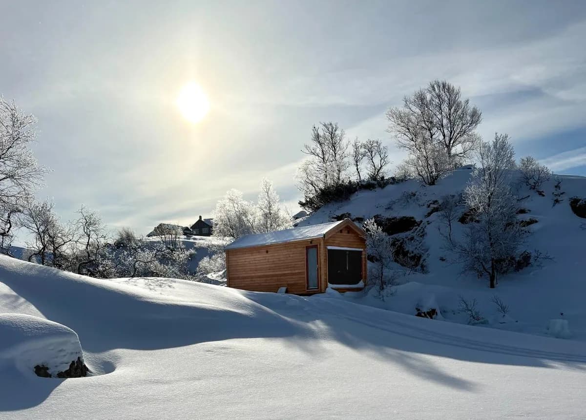 Badstue Helga den lune i vinterlandskap i Sirdal med trekledning og snødekt fjellterreng