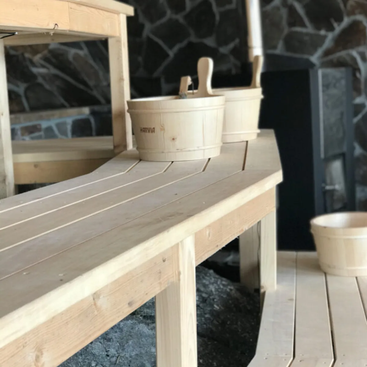 Interiør av Arctic Sauna i Skarsvåg med trebenker, Harvia-bøtte og steinvegg