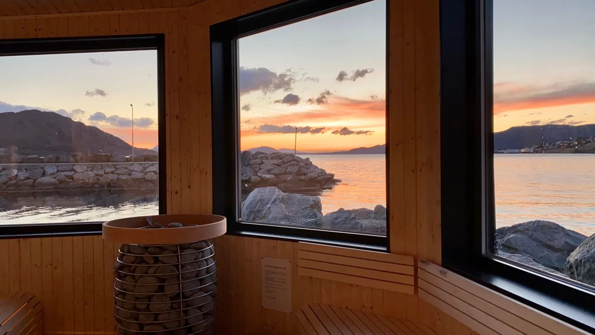 Interiør i Fjølg Sauna i Sykkylven med solnedgang over fjorden gjennom store vindauge
