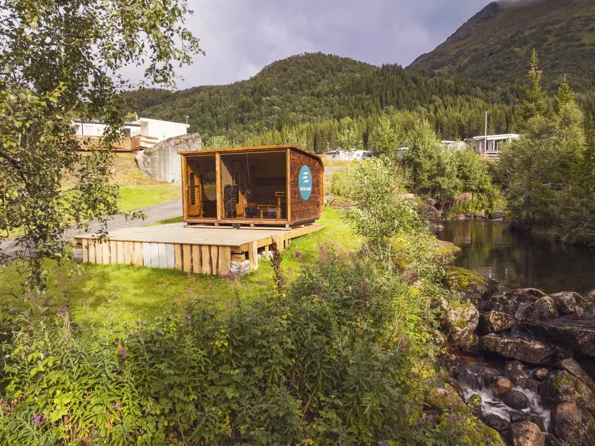 Aurora Sauna Vesterålen sett fra luften ved elv i Tengelfjord, omgitt av grønn natur