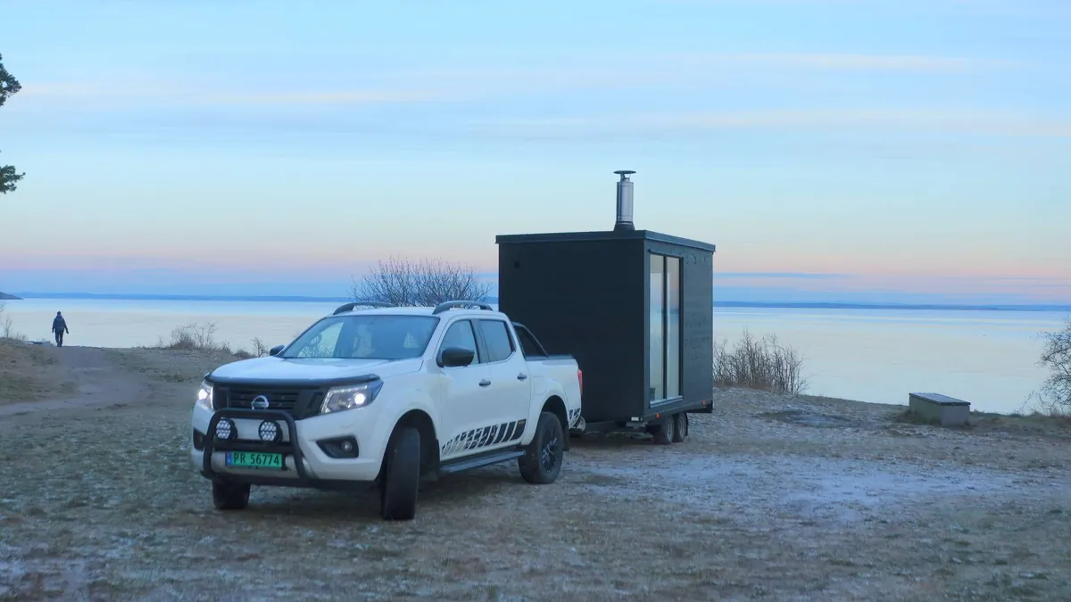 SaunaKing – eksterior Sort mobil badstuehenger tilkoblet en pickup ved vannkanten i skumring
