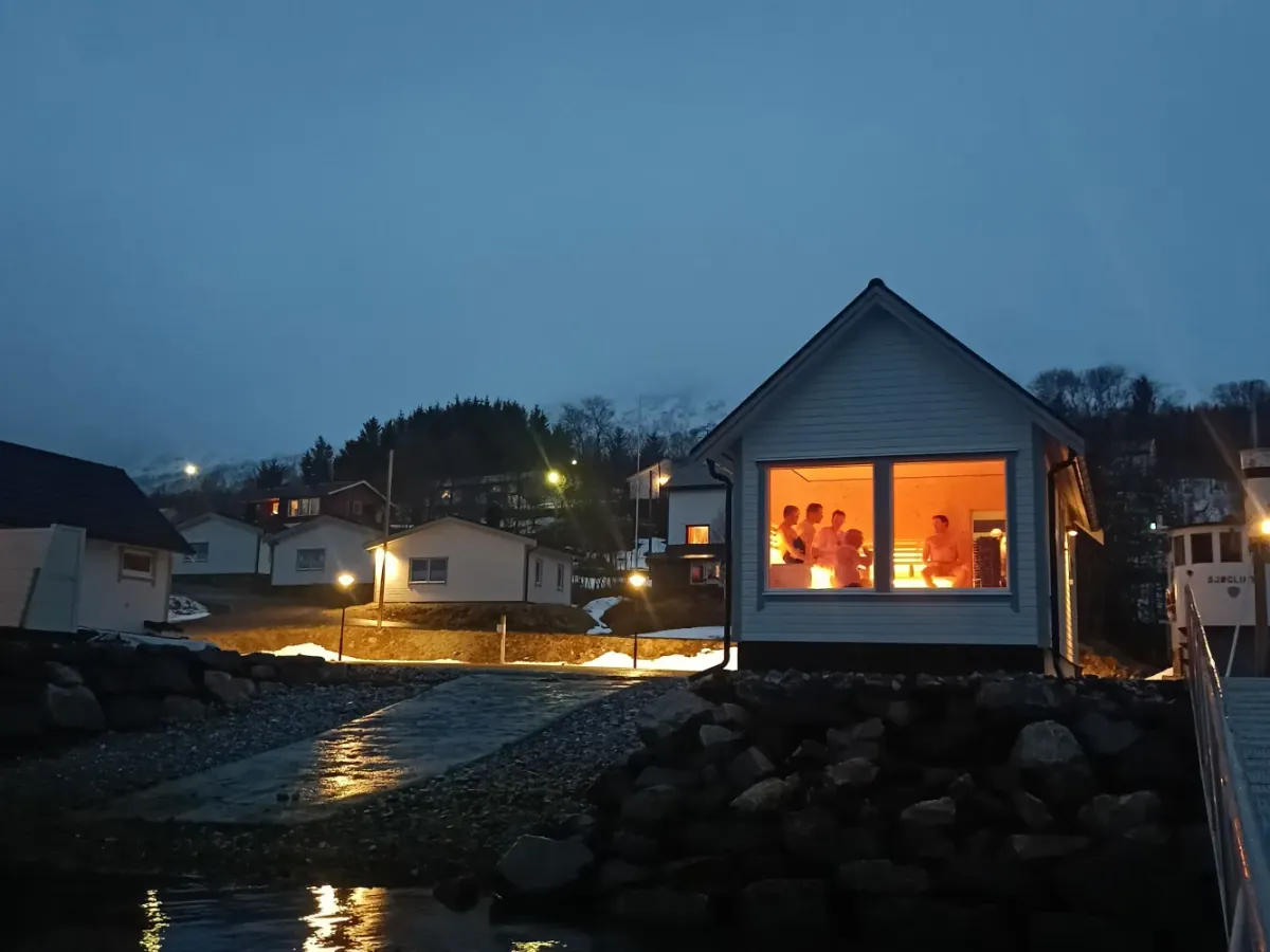 Senja by Heart Sauna i Torsken sett utenfra om kvelden med opplyste vinduer, gjester inne og fjorden i forgrunnen