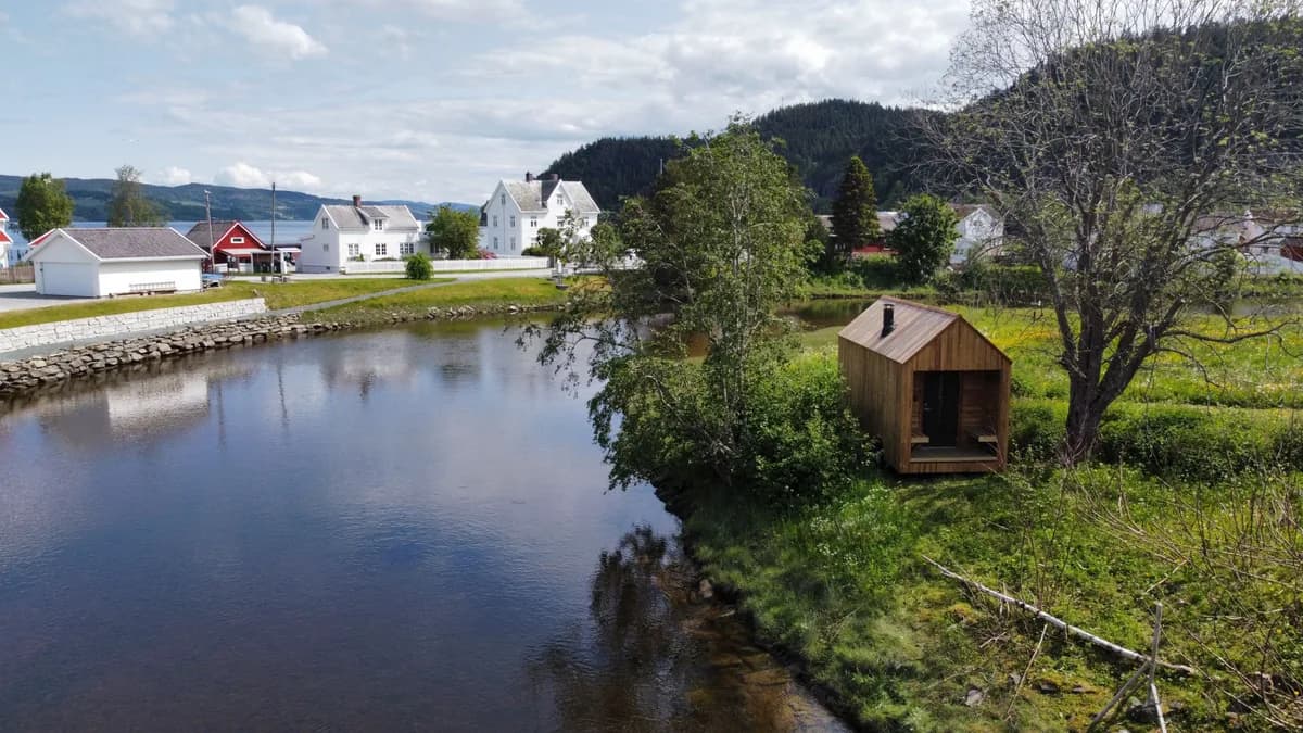 Naust Sauna i Børsa ved elven, trebygget badstue omgitt av grønt landskap og fjell