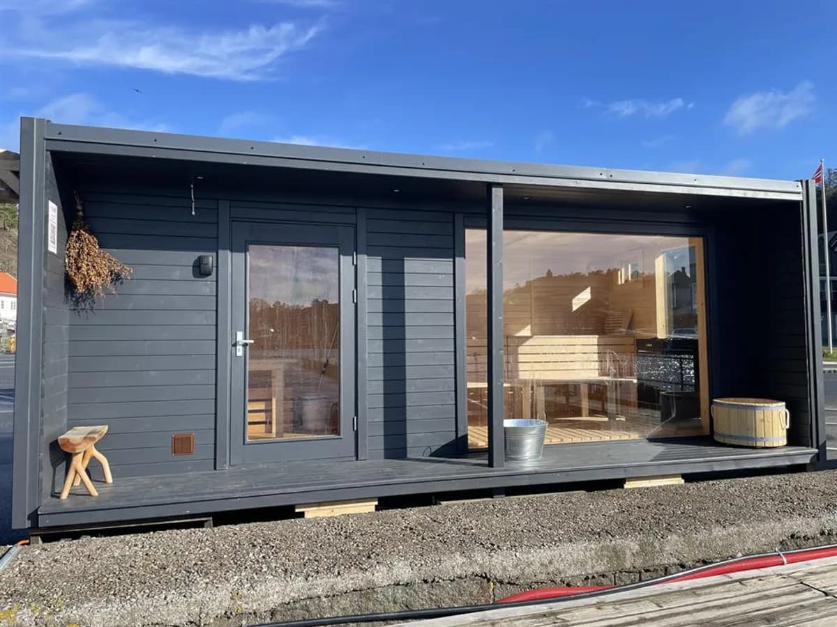 Kur Sauna Ula sett utenfra med mørk grå panel, glassdører og terrasse ved sjøen