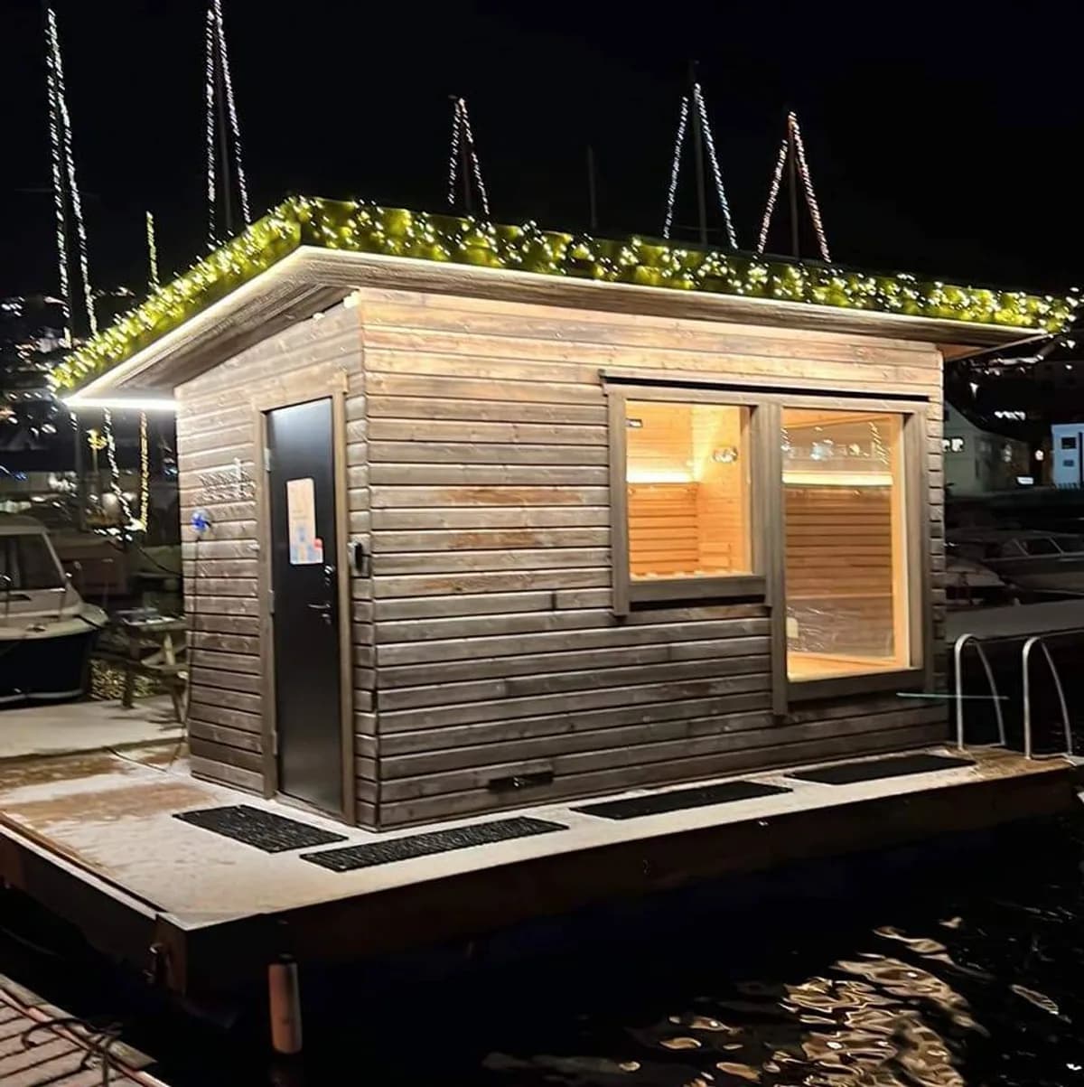 Ulstein Havsauna i Ulsteinvik, flytende badstu med lyslenker ved marinaen om kvelden