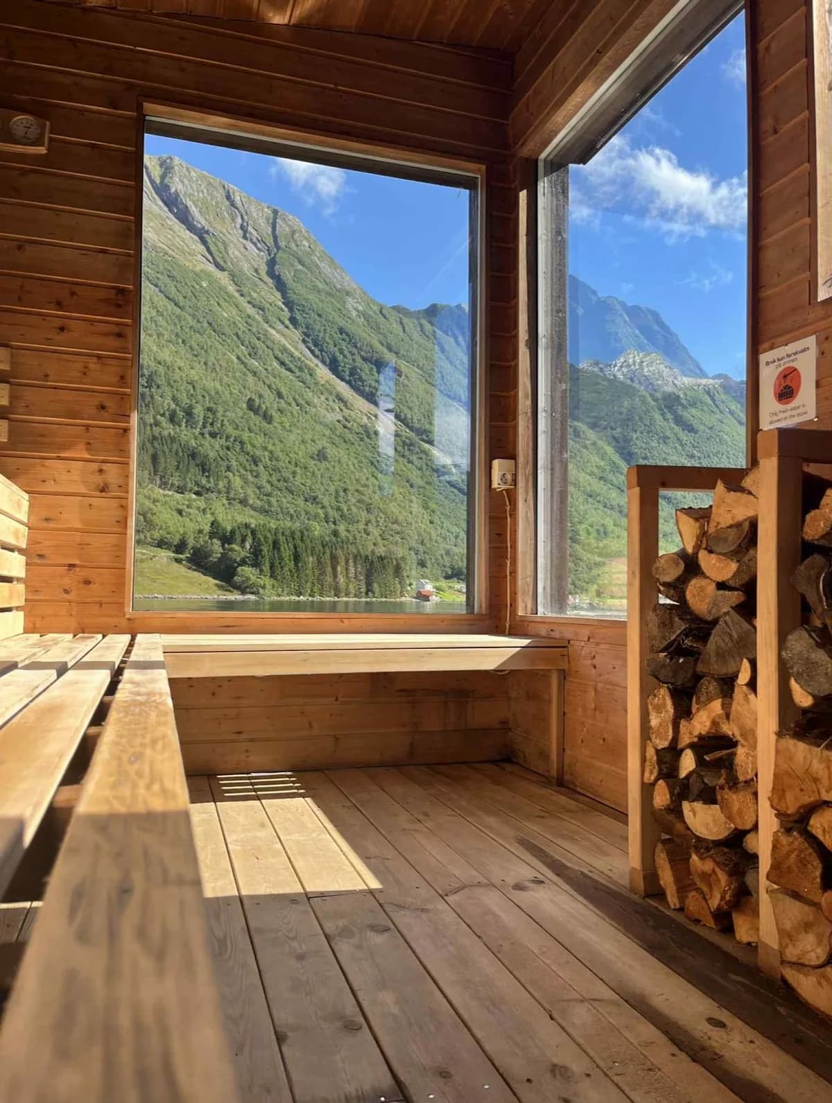 Interiør i Fjordbu Sauna Urke med trebenkar, vedovn og panoramautsikt mot fjell i Hjørundfjorden