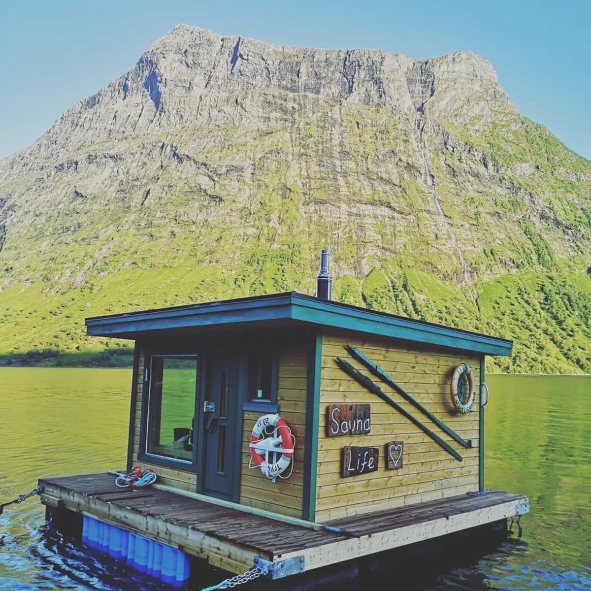 Urke Fjordsauna flytende badstue i Hjørundfjorden med fjell i bakgrunnen, sommer
