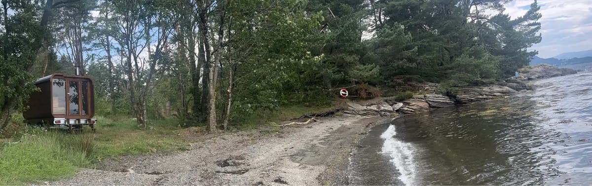 Bjoa Badstua ved stranden i Vedvikjo med trær og fjordutsikt