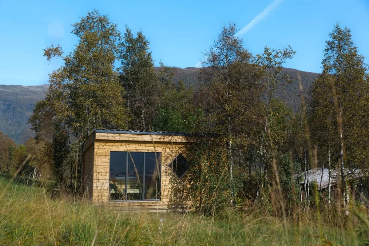 Fjellsauna Myrkdalen i Vossestrand, trebygg med store glassvinduer omgitt av bjørketrær og fjell